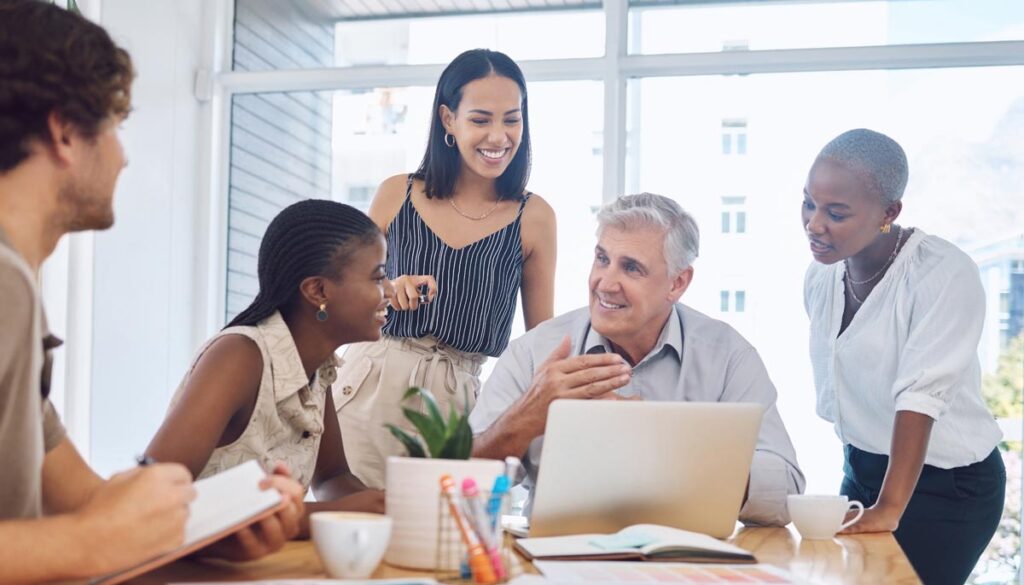 A diverse and multigenerational group of coworkers collabrating around a conference table. 