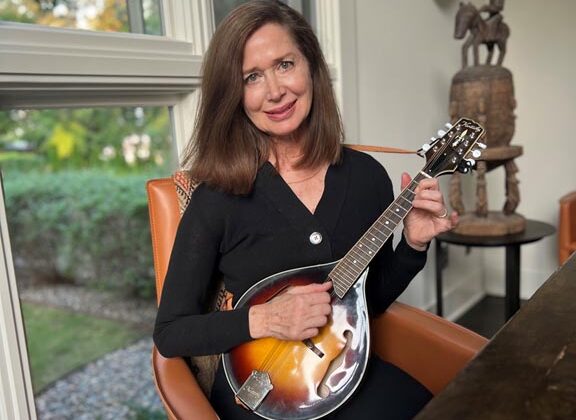 Executive Consultant Jill Harmon Seated In Her Home Holding Her Mandolin Musical Instrument.