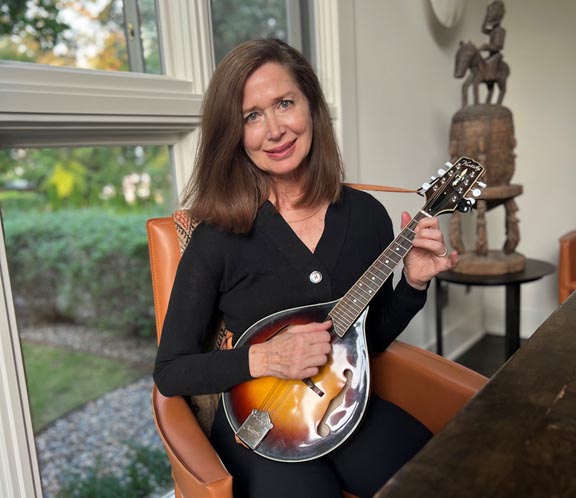 Executive consultant Jill Harmon seated in her home holding her mandolin musical instrument.