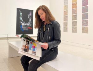 Jill Harmon seated on modern white bench in art gallery looking at artistic book of photos. 