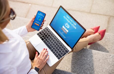 Women In Business Attire White Shirt Tan Pants Holding Laptop And Smartphone, Sitting Outside On Steps.