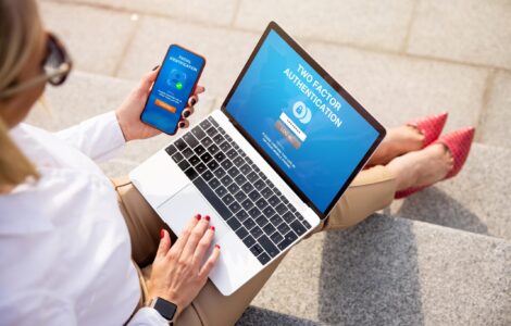 Women In Business Attire White Shirt Tan Pants Holding Laptop And Smartphone, Sitting Outside On Steps.
